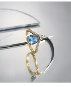 Macro shot of V-shaped gold ring with pear-cut blue gemstone and side pavé zircon details