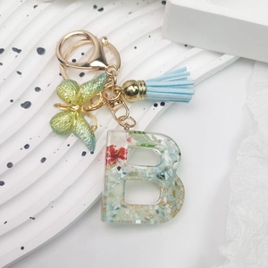 Macro view of crystal resin letter B keychain with dried flowers and green butterfly charm