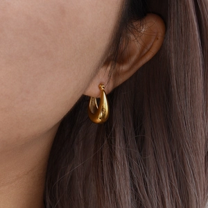 Detail of a polished gold hollow U-shaped earring worn by a model in soft lighting