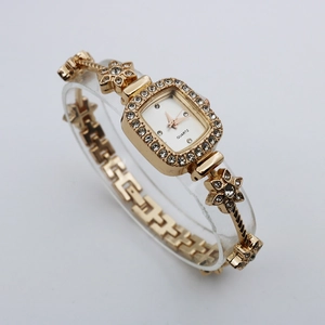 Detail of square gold bracelet watch featuring a crystal bezel and floral links on a stand