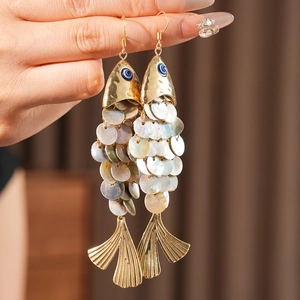 Detail of fish earrings with mother-of-pearl scales and blue enamel eyes held by hand