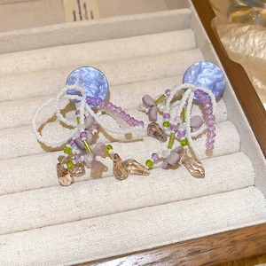 Close-up of elegant beaded tassel earrings with purple resin disc and crystal drops charms
