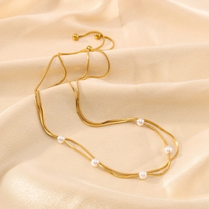 Zweilagige goldene Schlangenkette mit weißen Perlen auf champagnerfarbenem Seidenstoff