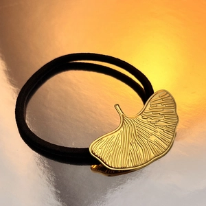 Elegant gold ginkgo leaf hair tie with black elastic band on a gradient background