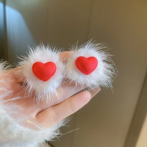 Close-up of fluffy white faux fur pom-poms with matte red heart charms on earrings