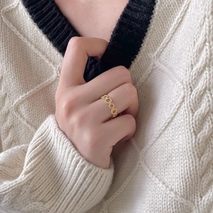Detailed close-up of a hollow chain link style gold ring worn with a white knit sweater