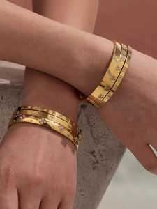 Macro detail of gold geometric bracelets with zircon inlay on a textured stone background