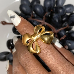 Detailed view of a gold-plated bow ring worn on finger with grapes background