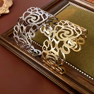 Detailed view of hollowed floral gold and silver open cuff bracelets on a wooden frame