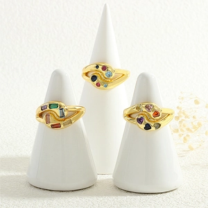 Detailed view of three gold rings with multi-colored gemstones on white ring cones