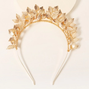 Detail view of a golden leaf-shaped headband with metallic texture on a beige background