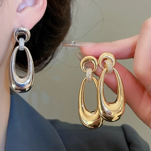 Detailed view of large teardrop earrings in polished gold and silver with zircon accents