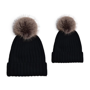 Detail of adult and child black knit beanies with fluffy brown faux fur pom-poms