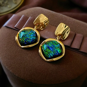 Macro-detail van vintage oorbellen met groenblauwe harsstenen en goud gehamerd metaal