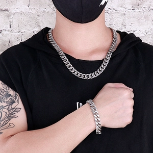 Detail of silver Cuban chain necklace and bracelet set worn against white brick wall