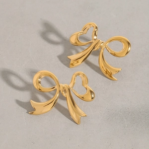 Detailed close-up of bow-shaped golden earrings with hollow heart design on grey surface
