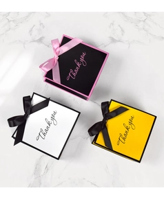 Overhead view of three square gift bags with satin ribbons and Thank You gold lettering