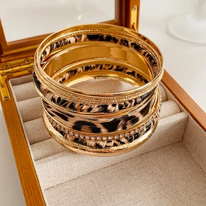 Detail of leopard print bangles and white rhinestone rings in a wooden jewelry box