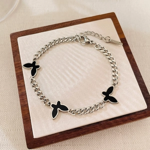 Detail of silver stainless steel chain bracelet with black butterfly charms on wood tray