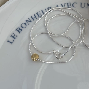 Minimalist S925 sterling silver snake chain necklace with single gold bead on white porcelain