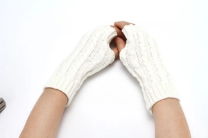 Close-up of white knitted fingerless gloves showing classic thick cable knit texture and pattern
