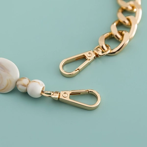 Macro detail of golden metal spring clasps and marble-textured resin beads on a chain