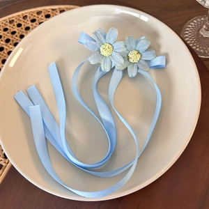 Detail of light blue floral hair clip with ribbons on a ceramic plate over a wooden table