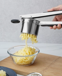 Action shot of stainless steel potato ricer pressing mash into a glass bowl with handle