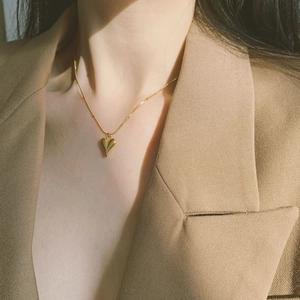 Minimalist gold titanium steel heart necklace shown on model wearing a camel suit jacket