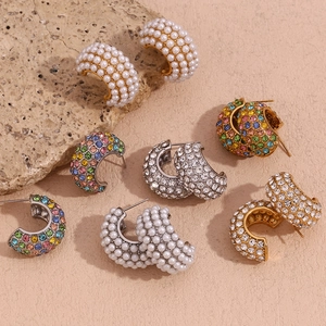 Detail of C-shaped earrings with pearls and colorful zircons on pink background