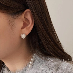 Detail of silver heart stud earring with pleated texture and zircon on model
