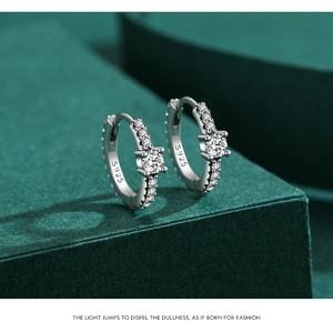 Close-up of S925 sterling silver hoop earrings with clear stones on green surface