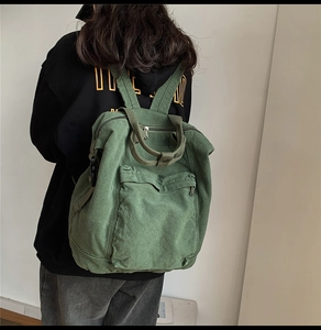 Detailed back view of a large green washed canvas backpack worn by a model in a minimalist setting