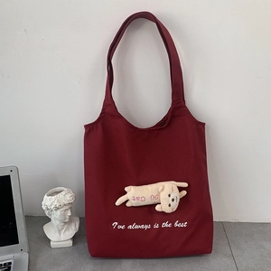 Detail of burgundy canvas tote bag featuring plush cat doll and white script text