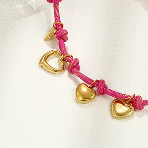 Macro detail of a pink braided bracelet featuring multiple gold heart-shaped pendants