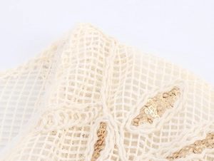Macro detail of apricot mesh fabric with intricate gold sequin embroidery pattern