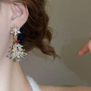 Close-up of gold snowflake and Christmas tree pearl tassel earrings on model