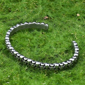 Close-up of punk style silver skull bangle on green moss background featuring gothic design