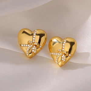 Macro detail of gold-plated heart earrings with zircon-studded bowknot on silk cloth