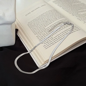 Artistic detail of silver flat snake chain necklace resting on a book and fabric