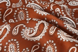 Close-up of caramel paisley silk scarf fabric showing premium satin texture and detail