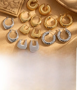 Detailed close-up of C-shaped textured gold titanium steel earrings on a sandy surface