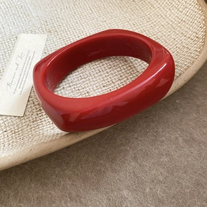 Detail of a thick square-edged bright red resin bangle on a textured ceramic tray