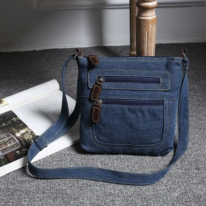 Detail of blue denim crossbody bag with multiple zippers and brown leather pullers