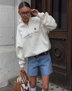 Detailed view of cream half-zip sweatshirt with collar and vintage blue lettering print