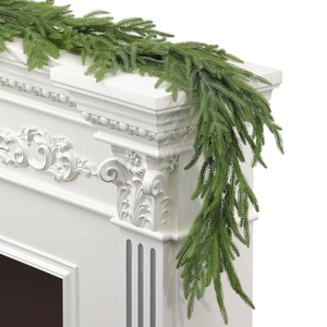 Realistic artificial Norfolk pine garland hanging on a white fireplace mantel decoration