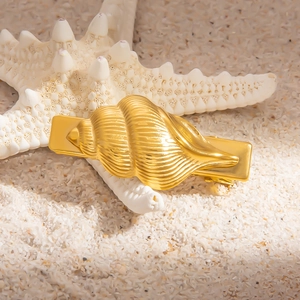 Golden seashell hair clip in stainless steel on sand with a decorative starfish