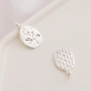 Detail of silver rose embossed pendant and woven textured charm on ceramic tray