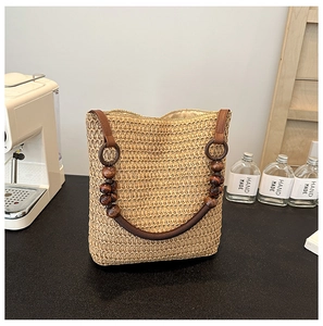 Detail of straw woven bucket bag with brown leather handle and decorative wooden beads