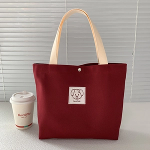 Detail of red canvas tote bag featuring a cute cartoon dog patch and magnetic metal clasp